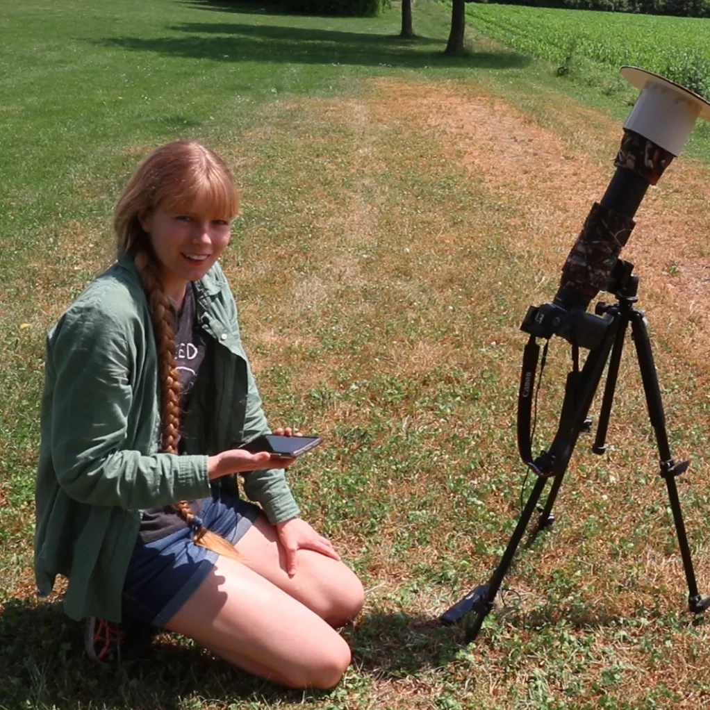 Sophie Paulin kniet neben ihrer Kamera mit Sonnenfilter auf dem Stativ